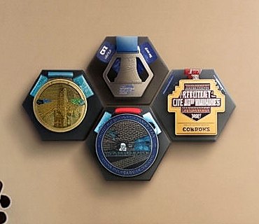 Hexagonal wall-mounted medal holders holding four race medals by their ribbons.