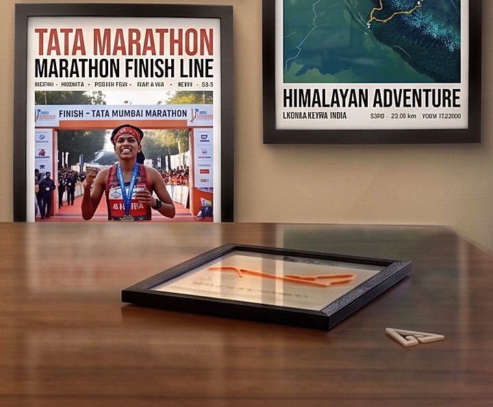 Coming soon: a race route 3D-printed in orange filament, mounted over a printed name in a black shadow-box frame, lying on a wooden desk.